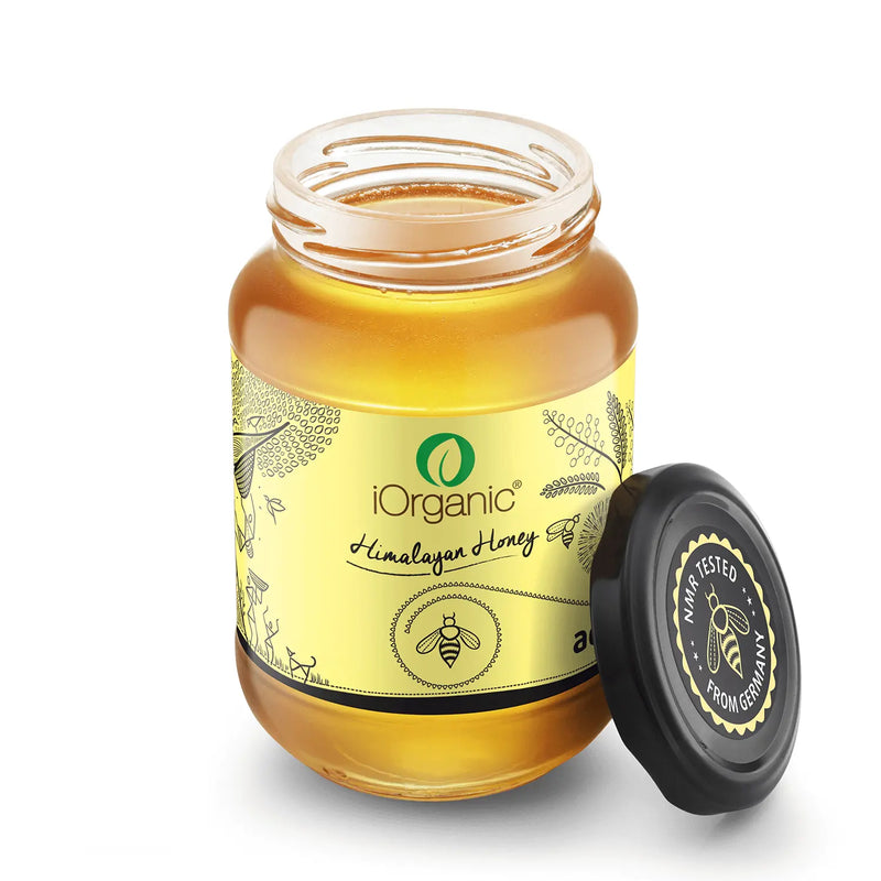 iOrganic Raw Acacia Honey jar open on a kitchen counter, showcasing the light, golden, unfiltered honey with a NMR tested seal for authenticity and purity.