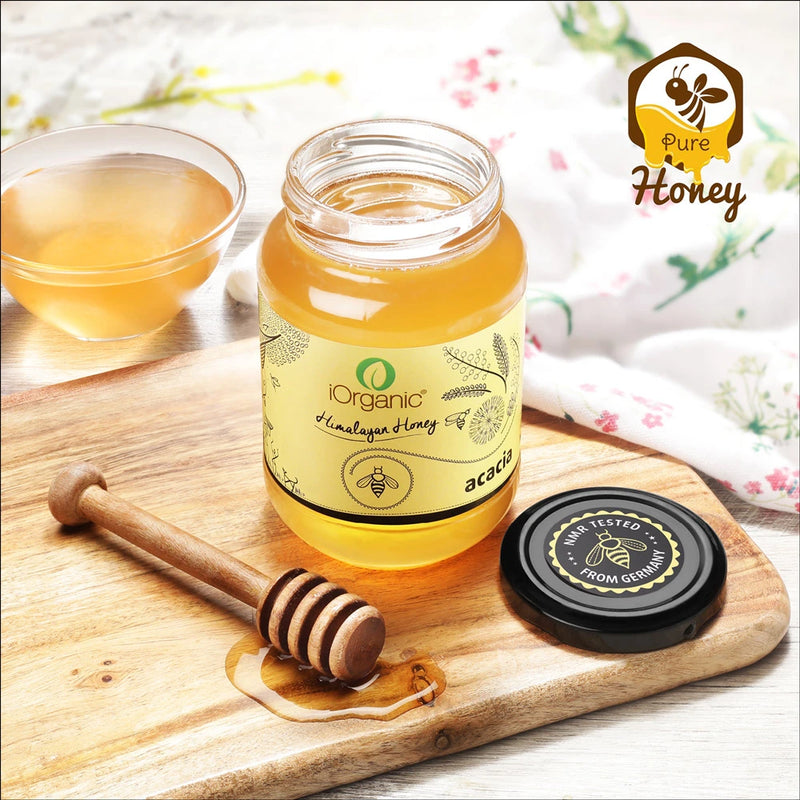 A wooden honey dipper drizzling iOrganic Raw Acacia Honey (500g), highlighting its pure, smooth, and luscious consistency. This ethically sourced honey from acacia blossoms in Kashmir is 100% natural and free from additives.