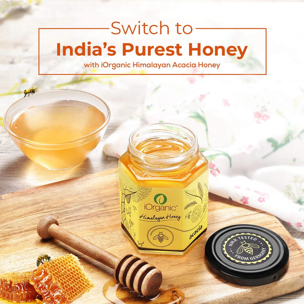 A luxurious jar of iOrganic Acacia Honey with natural honeycomb and a wooden dipper.